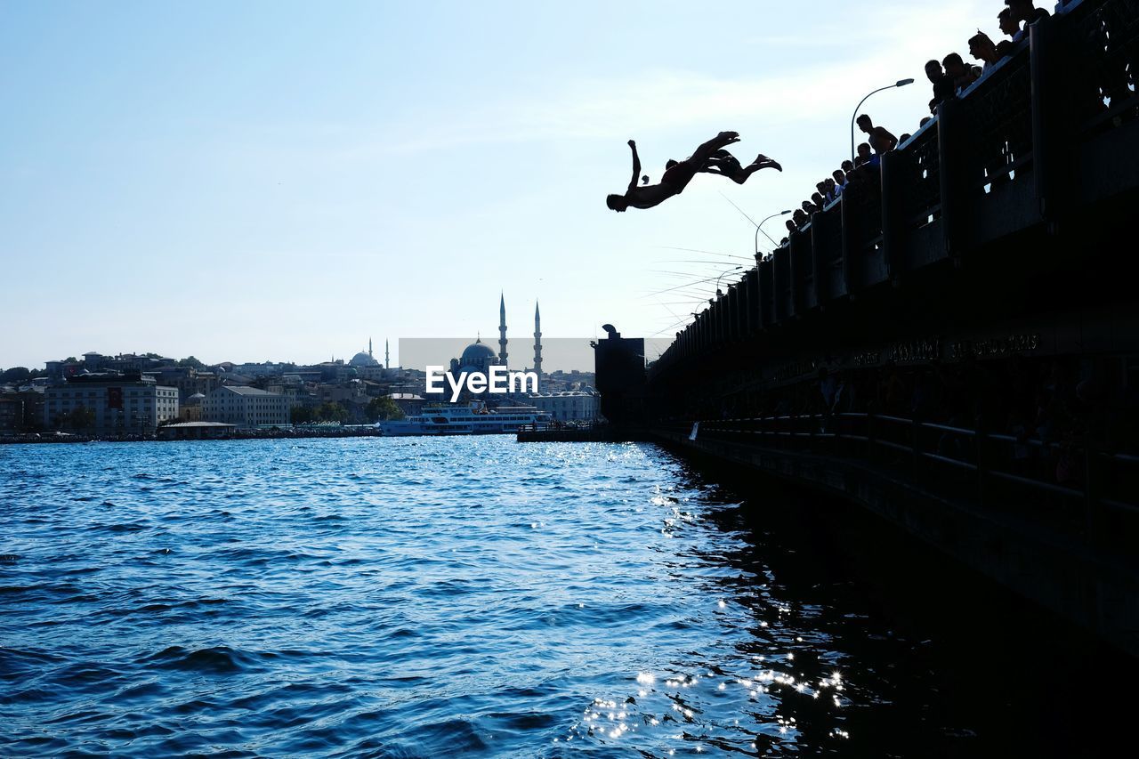 Silhouette children jumping in water at bosphorus strait against sky