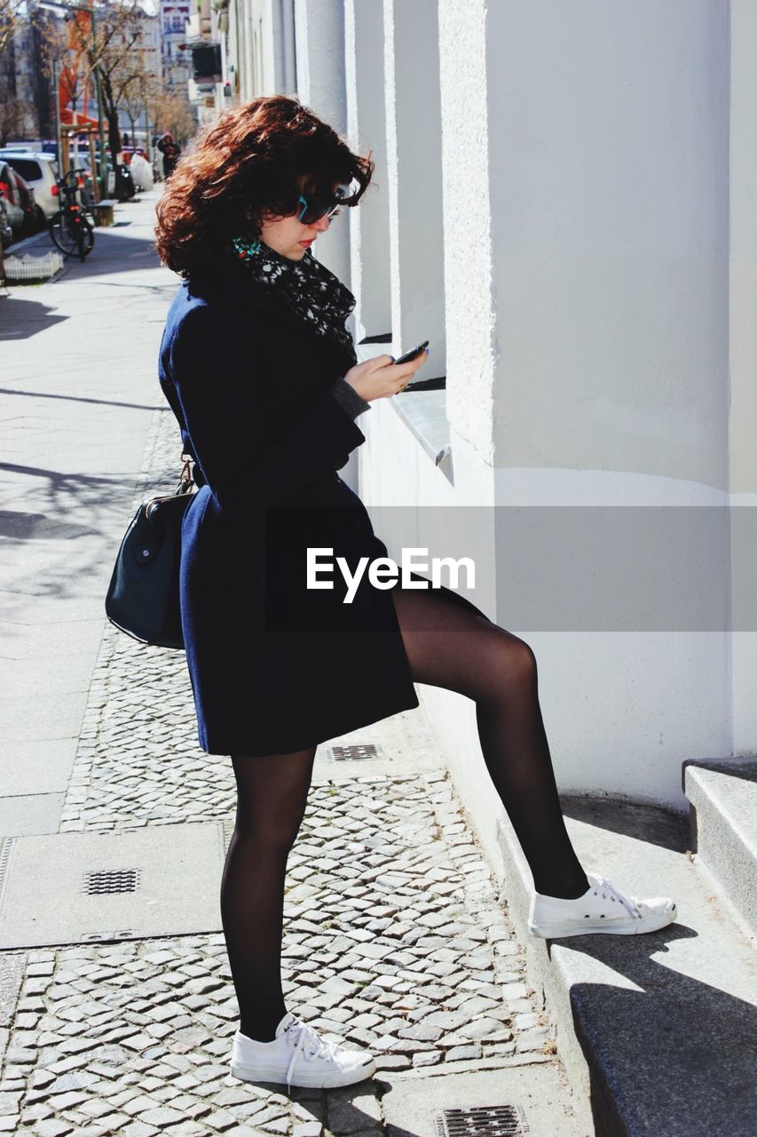 Full length of beautiful woman using phone on sidewalk in city