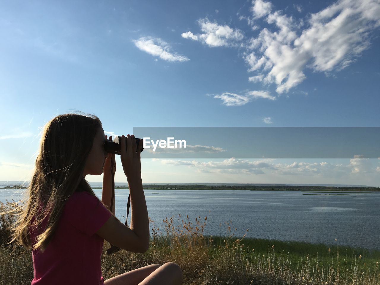 Woman looking at sea through binoculars against blue sky