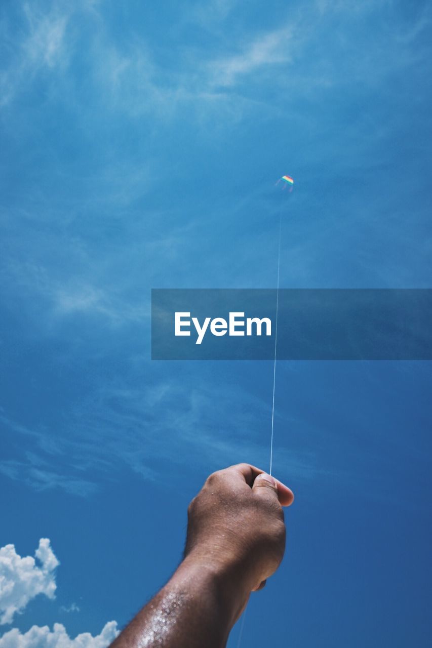 Cropped hand of man flying kite against blue sky