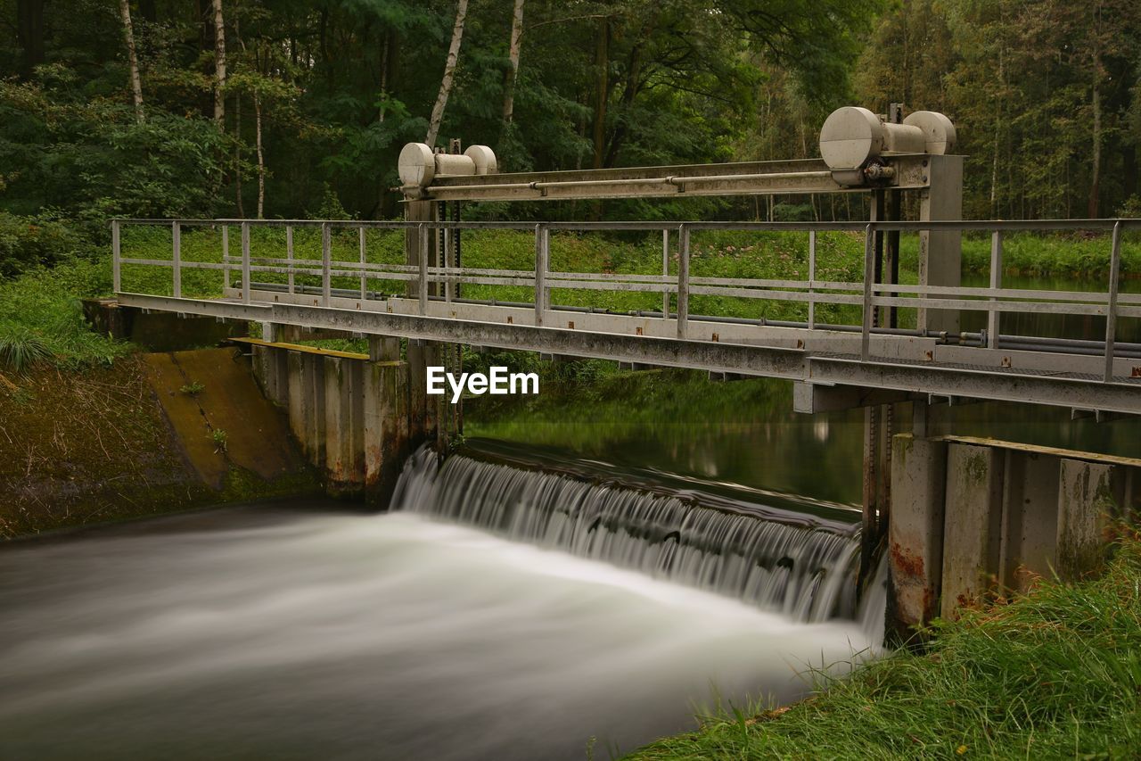 Footbridge over river against trees