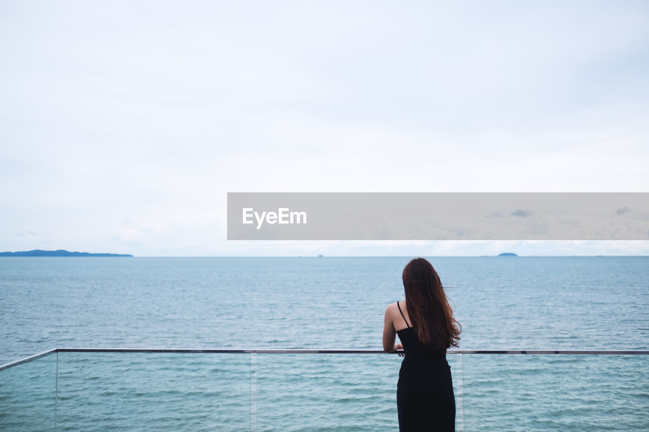 rear view of woman standing at sea against sky