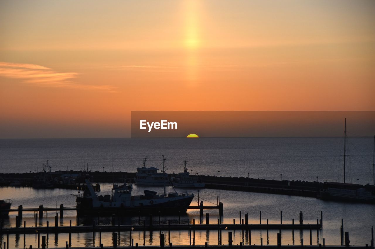 Scenic view of sea against orange sky during sunset seen from harbor