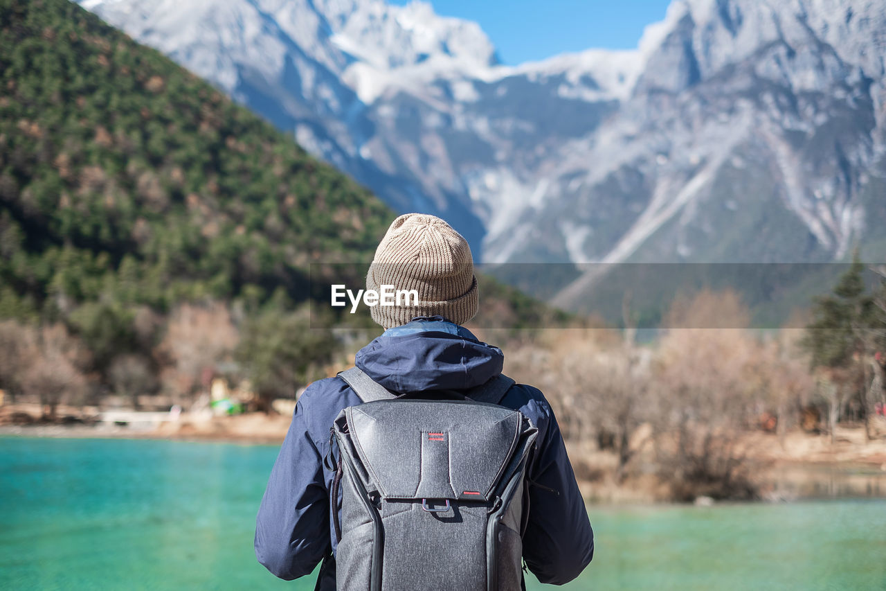 Rear view of woman standing by lake against mountains