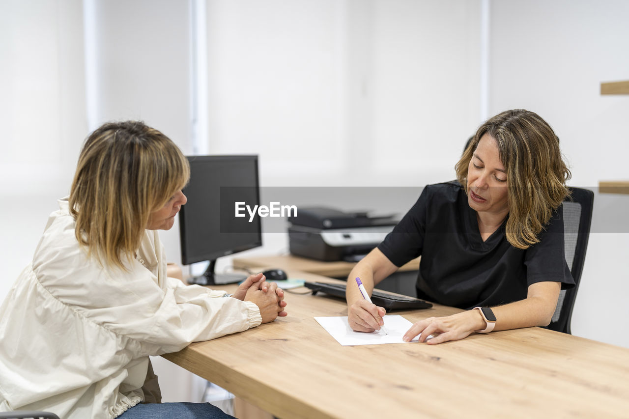 Doctor writing on paper while talking to patient in clinic