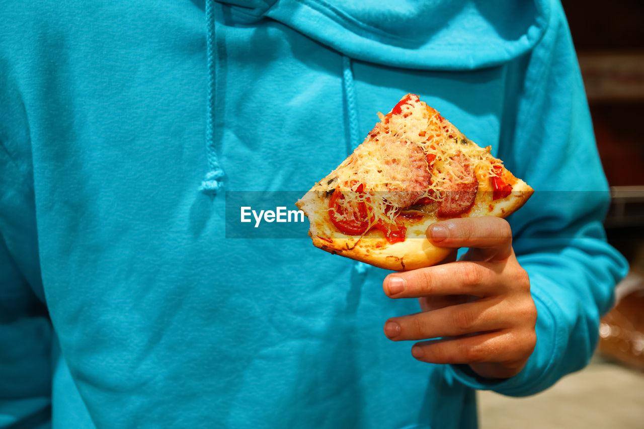 Male hand holding pizza slice. slice of pepperoni pizza in hand isolated on blue. concept 