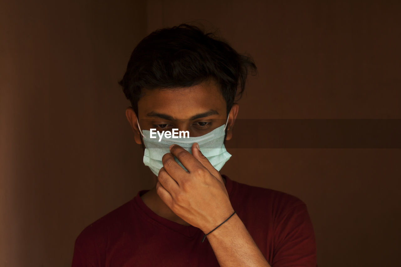 Close-up of young man wearing flu mask standing against black background