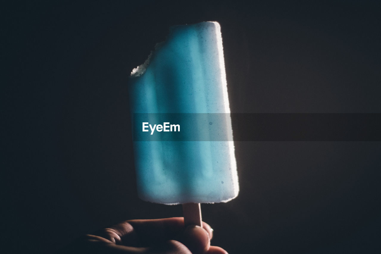 Close-up of hand holding ice cream against black background