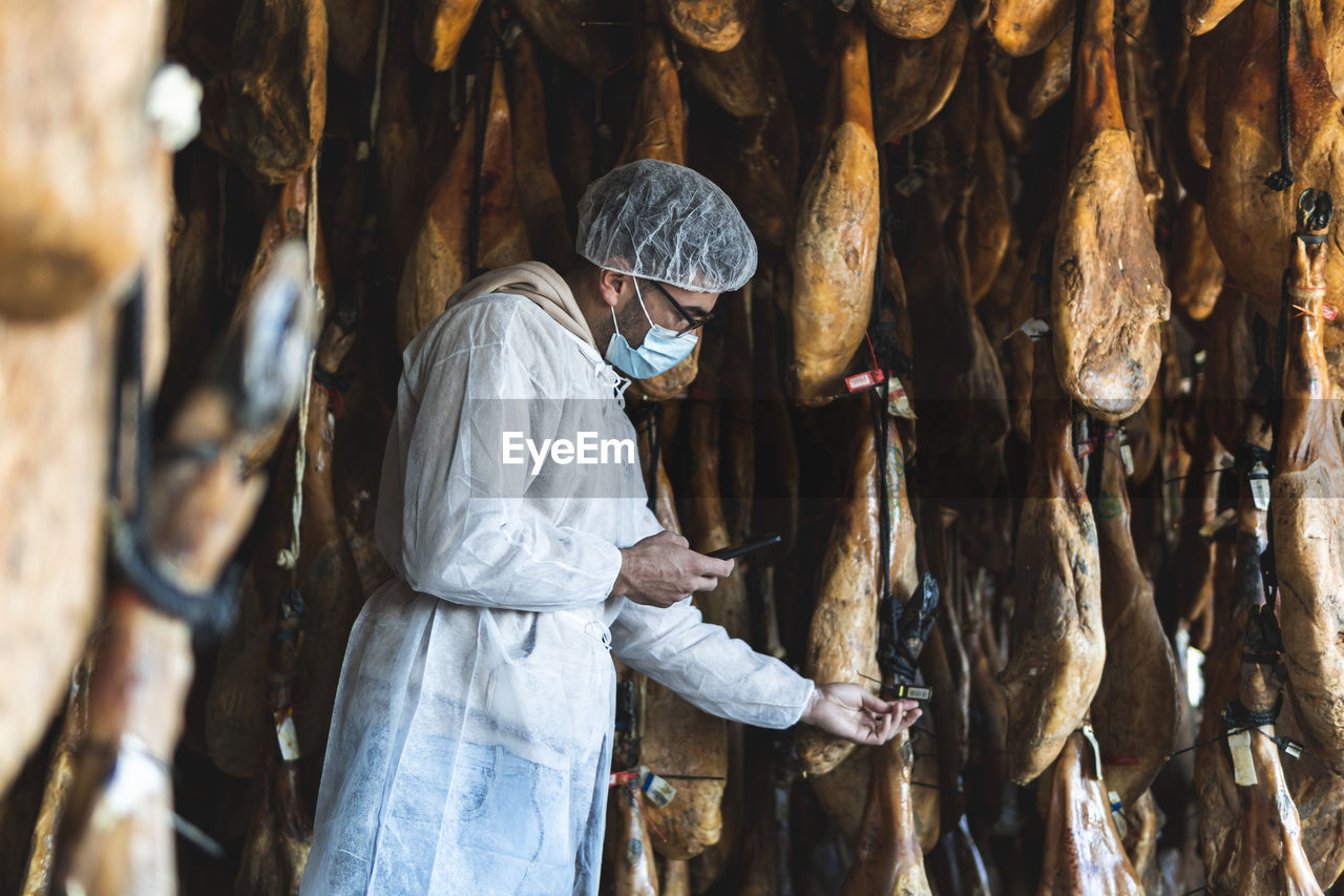 Employee choosing ham hanging in slaughterhouse