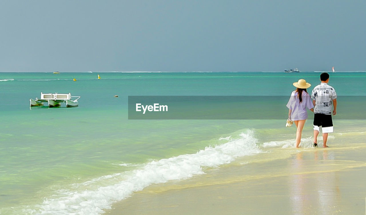 REAR VIEW OF FRIENDS STANDING ON BEACH