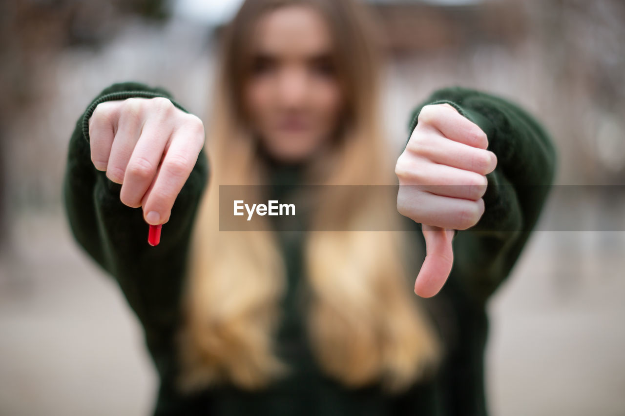 Close-up portrait of woman with pill showing thumbs down 