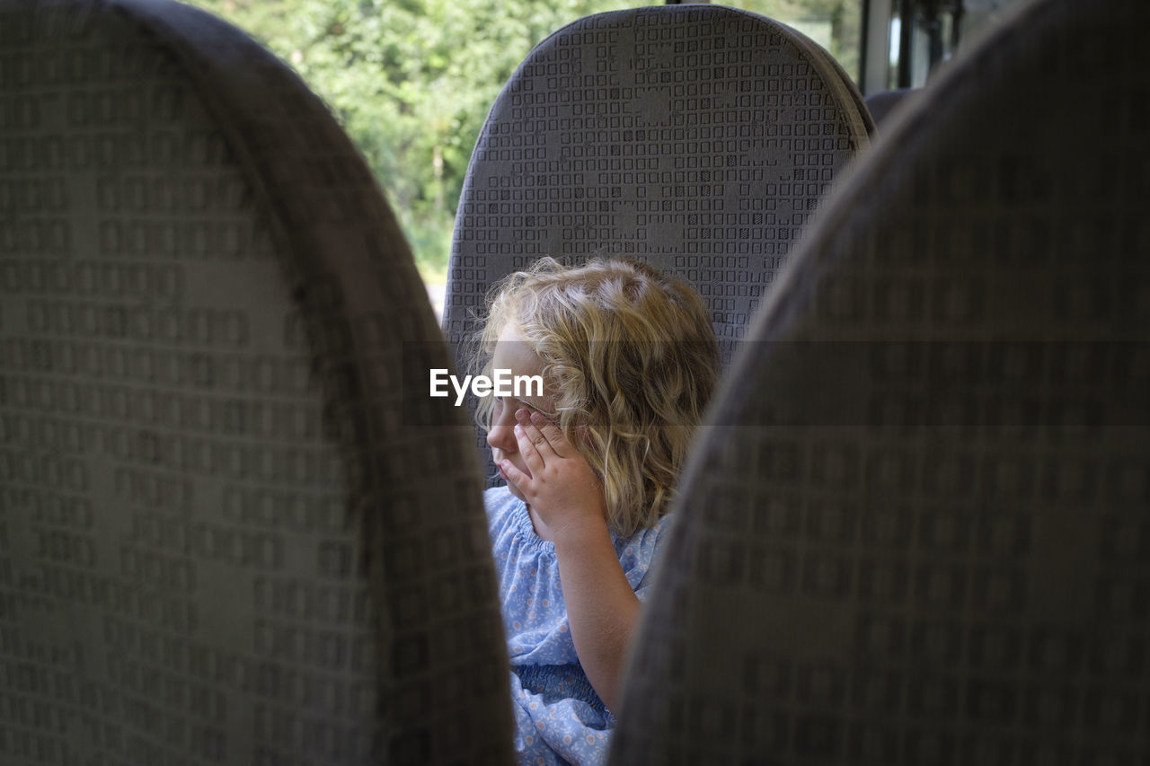 Young girl sitting on bus covering face with one hand