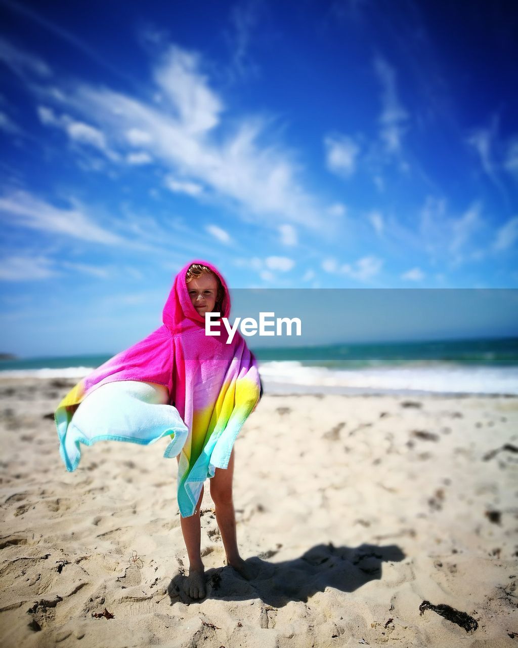 Boy covered with towel while standing at beach against sky