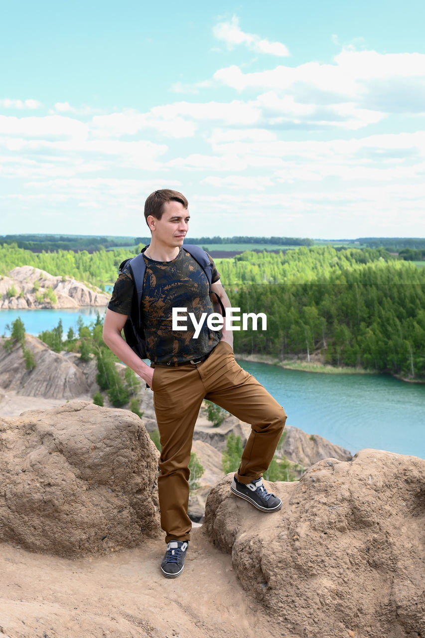 Male tourist stands on a rock above the river and forest.