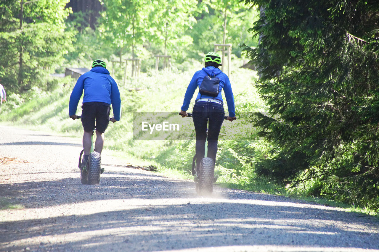 Rear view of people cycling walking on dirt road