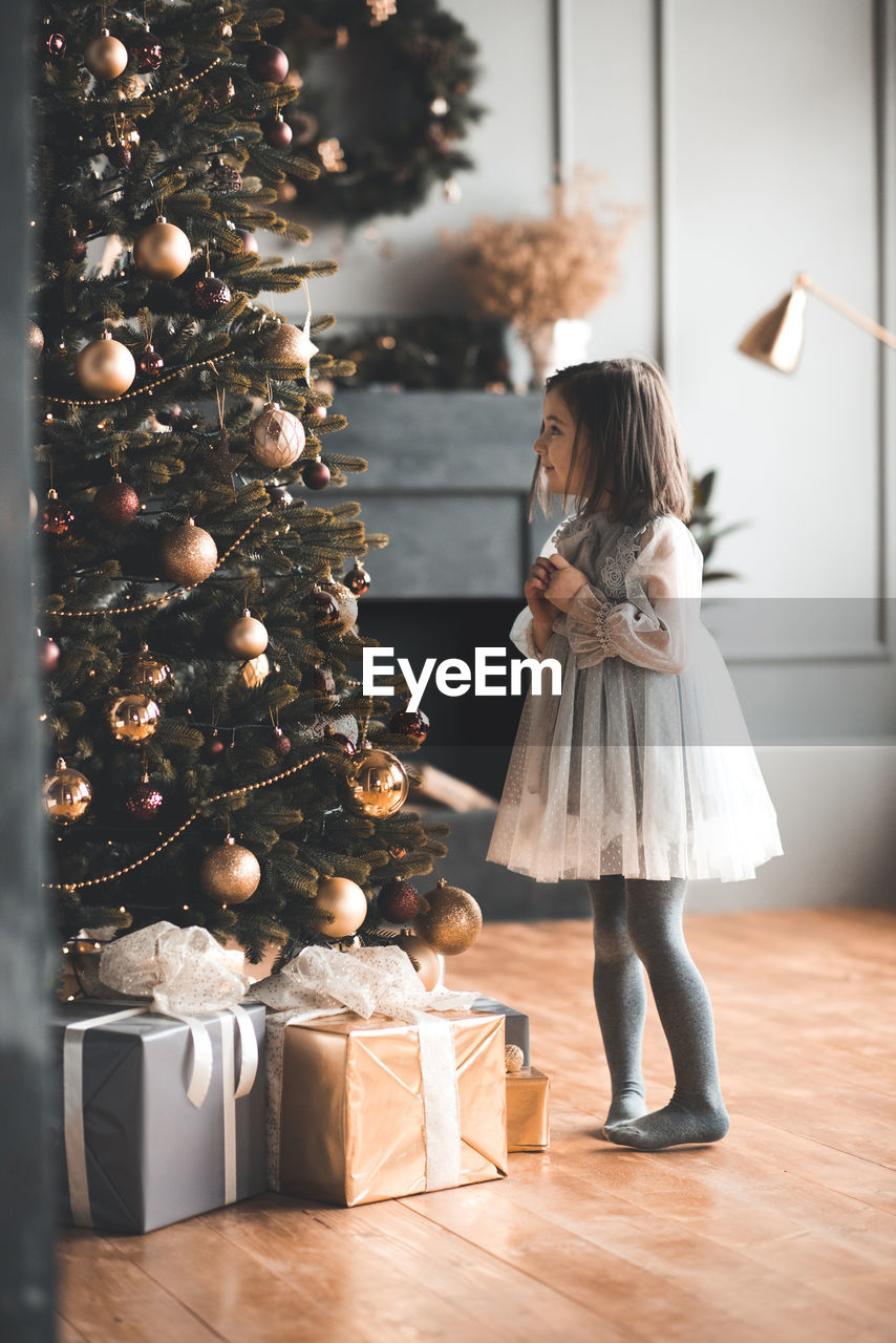 Full length of girl standing by christmas tree at home