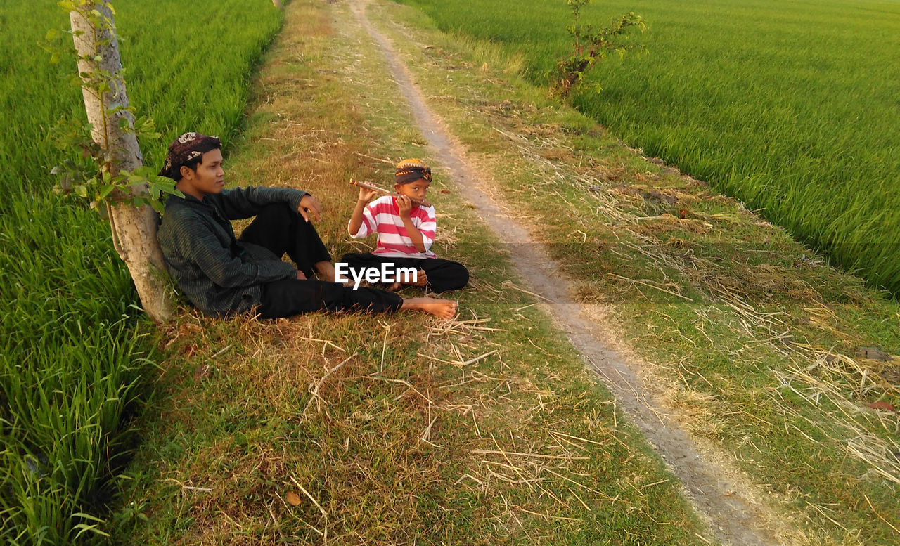 Father and son sitting on footpath amidst farm
