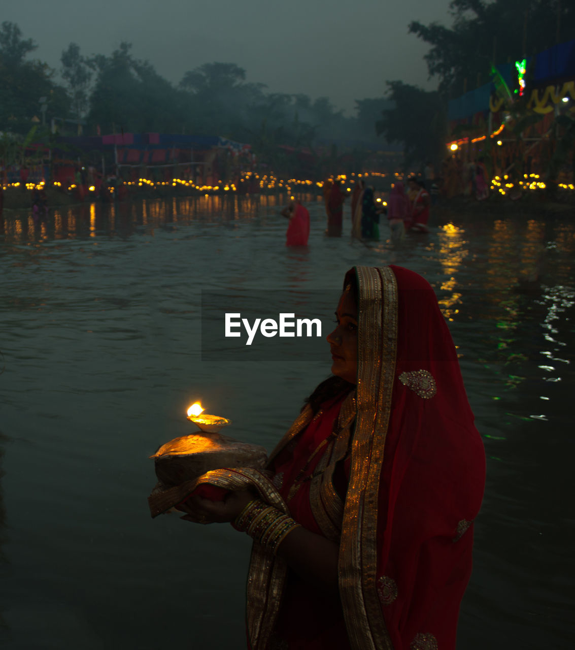 Woman standing with lit diya in river at night