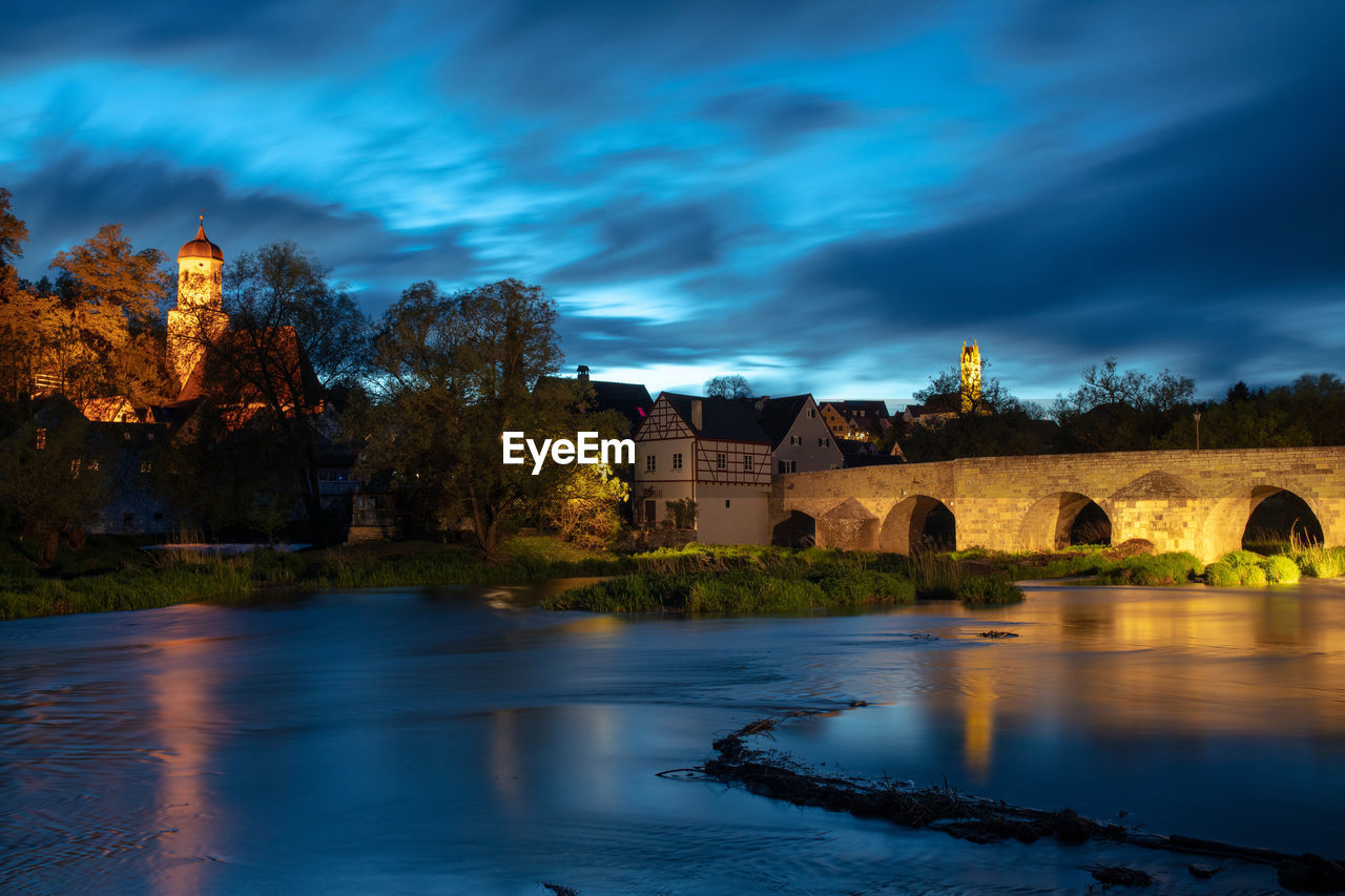 ARCH BRIDGE OVER RIVER AGAINST BUILDINGS AND TREES AGAINST SKY