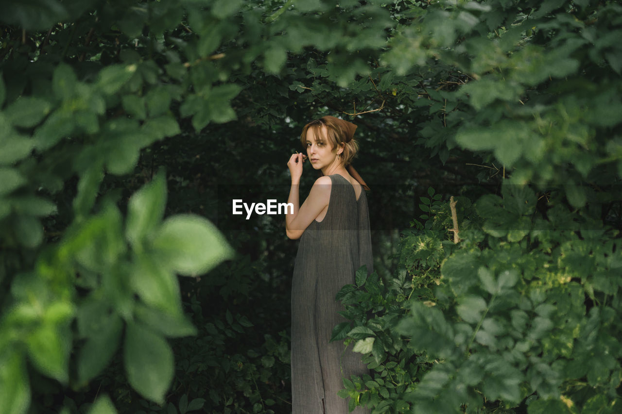 A woman stands in a dress in dense foliage