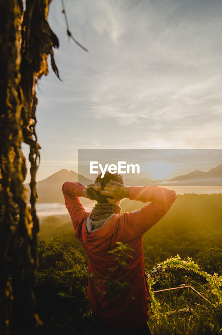 Rear view of man standing on mountain against sky during sunset