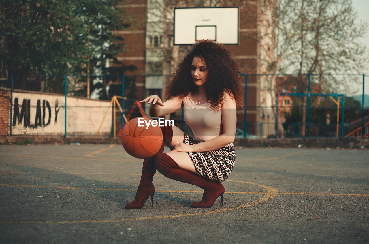 Beautiful young woman playing with basketball on court