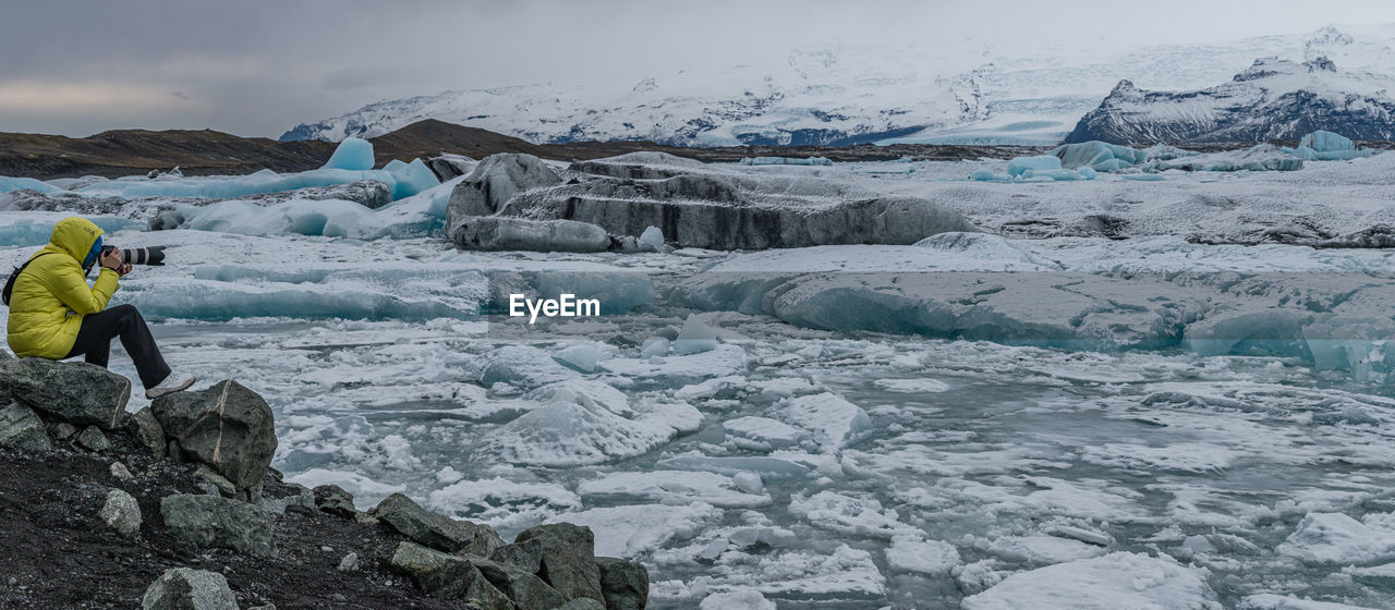 A photographer takes in a panoramic view of blue glacier ice floating in a lagoon