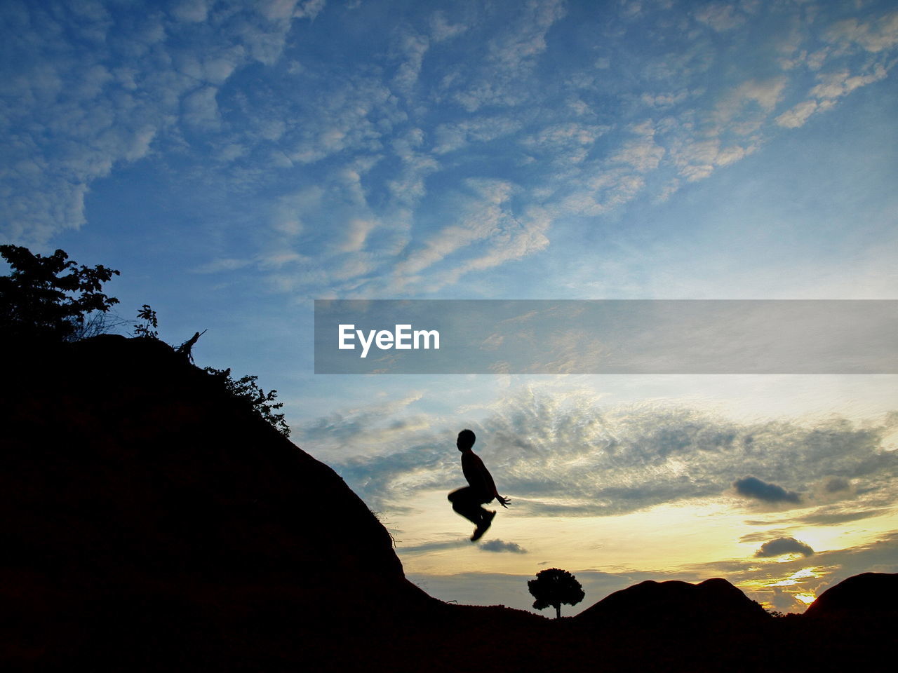 Silhouette man in mid-air against sky during sunset