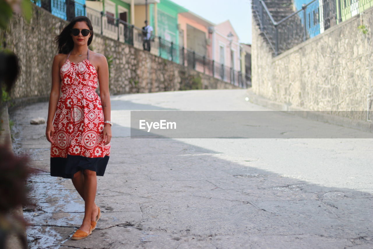 Full length portrait of woman standing on footpath in city