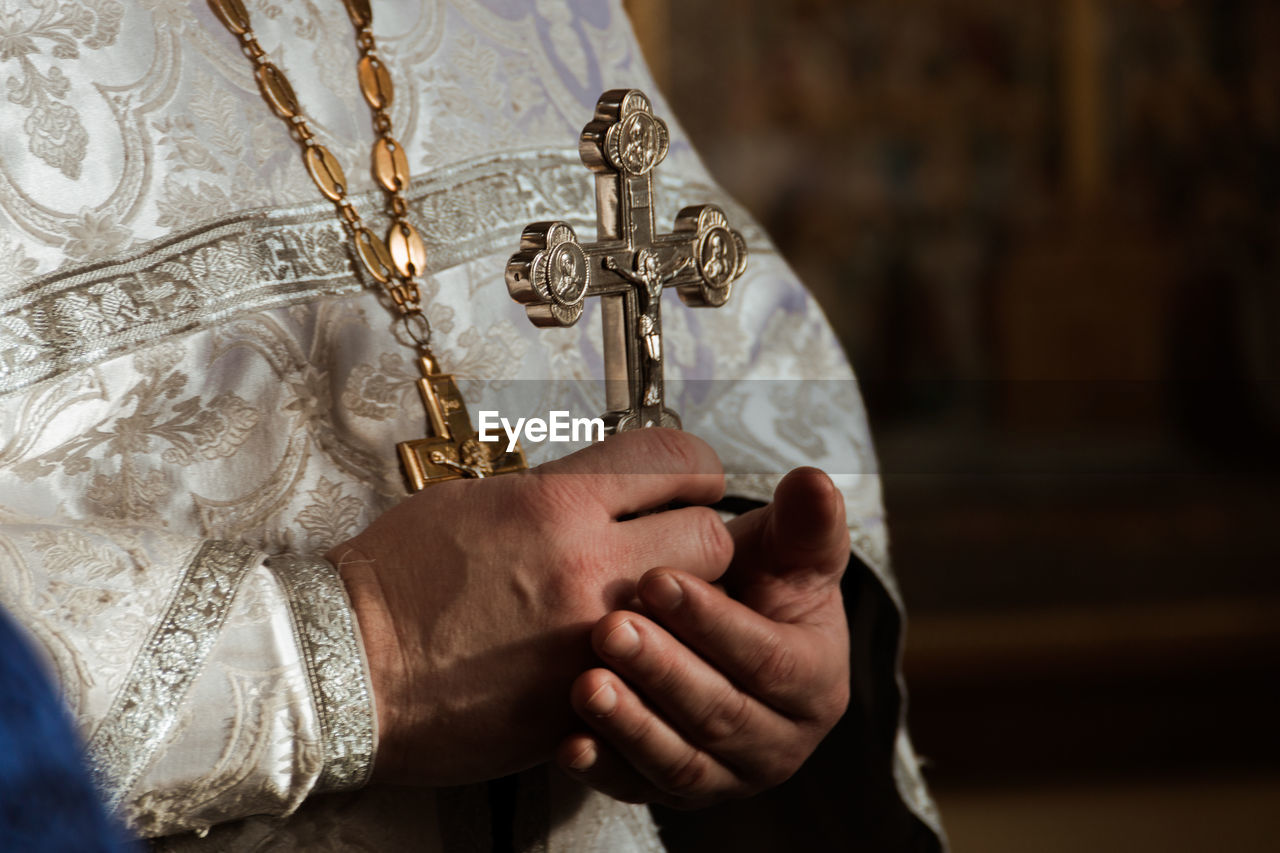 Midsection of priest holding cross in church