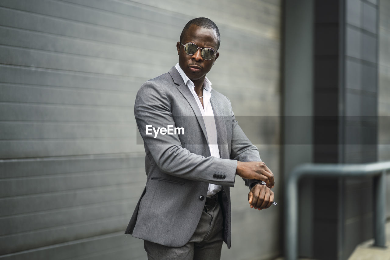 Masculine african american male executive in formal suit and sunglasses revising time on street