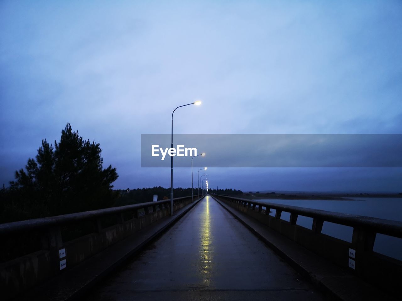 Street lights on bridge against sky at dusk