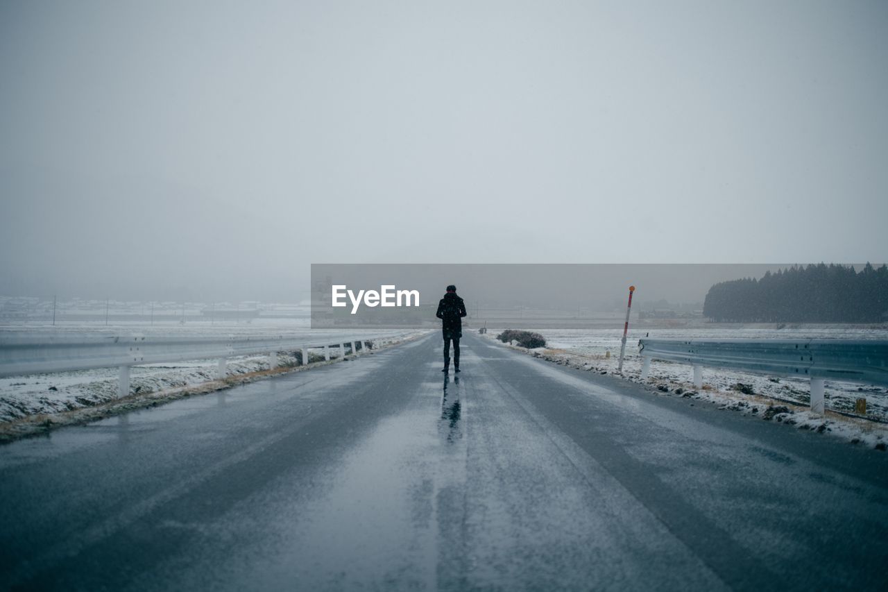 Person standing on empty road against sky during foggy weather