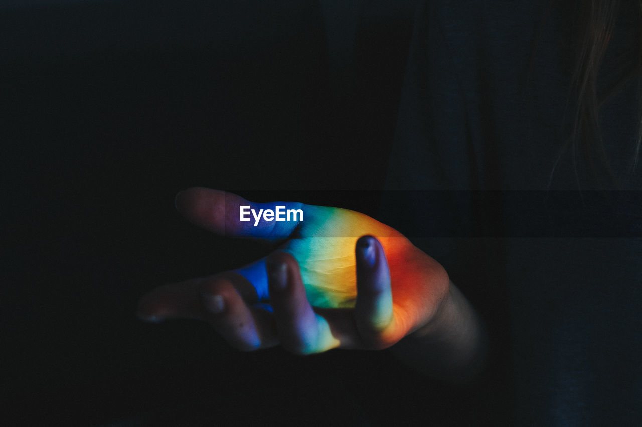 Cropped hand of person with spectrum against black background
