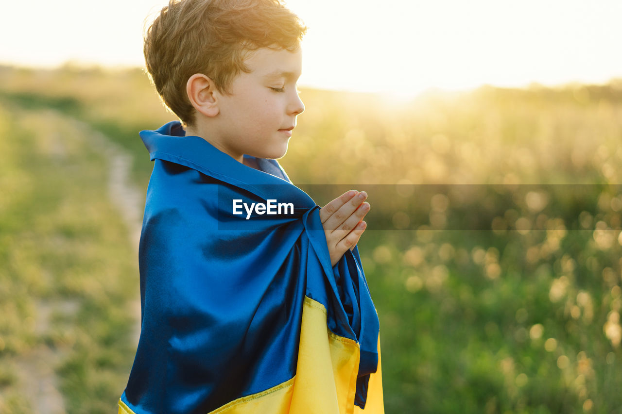 Ukrainian boy closed her eyes and praying to stop the war in ukraine in a field at sunset