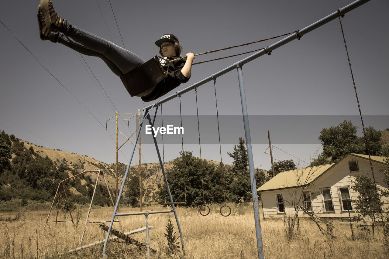 Low angle view of woman enjoying swing on grassy field against sky