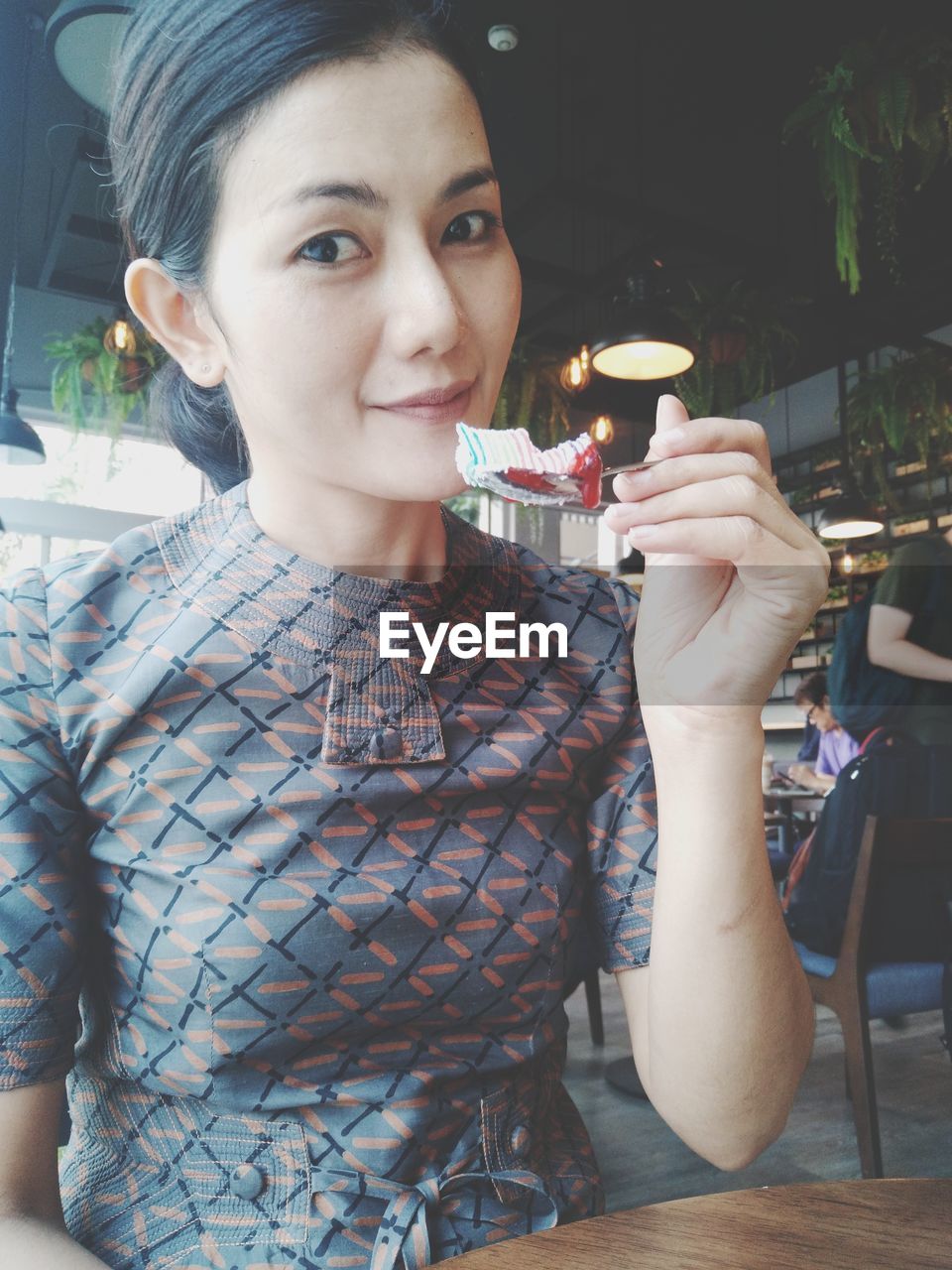 Low angle portrait of mid adult woman eating dessert while sitting in restaurant