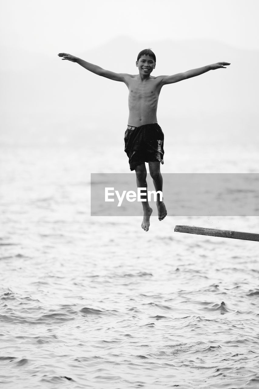 FULL LENGTH OF SHIRTLESS MAN JUMPING ON SEA