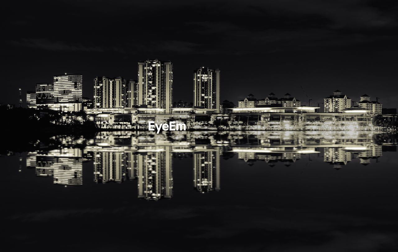 Illuminated buildings by river against sky at night