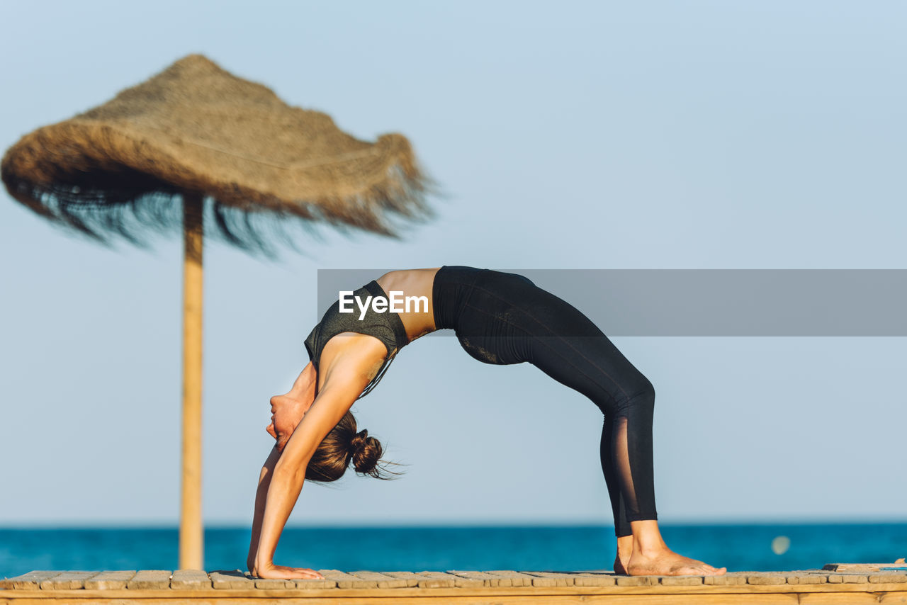 Full length of woman exercising at beach against sky