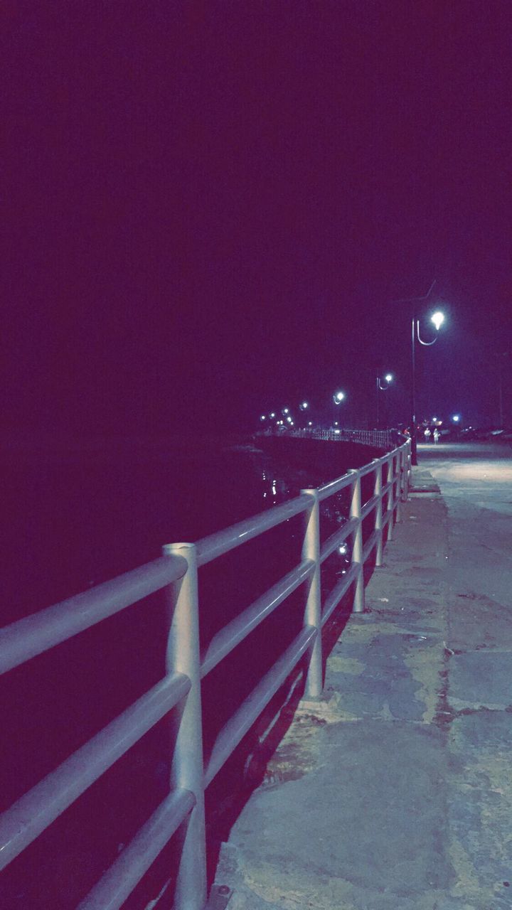 ILLUMINATED RAILING BY SEA AGAINST CLEAR SKY DURING NIGHT