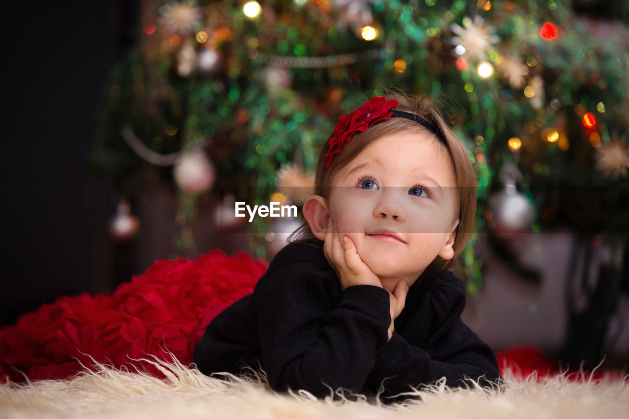 Thoughtful girl lying on rug against christmas tree at home