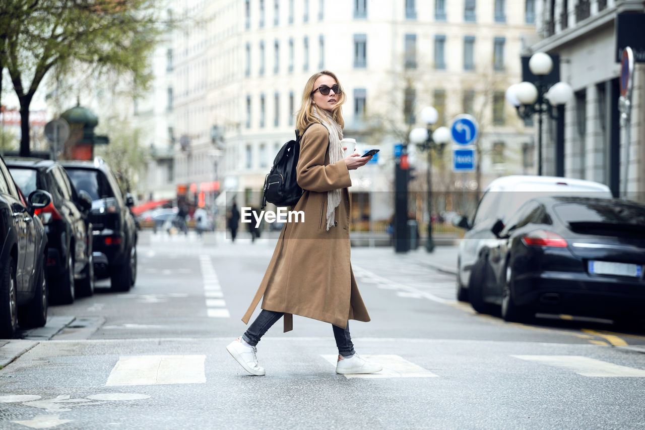 Woman with coffee cup using mobile phone on city street