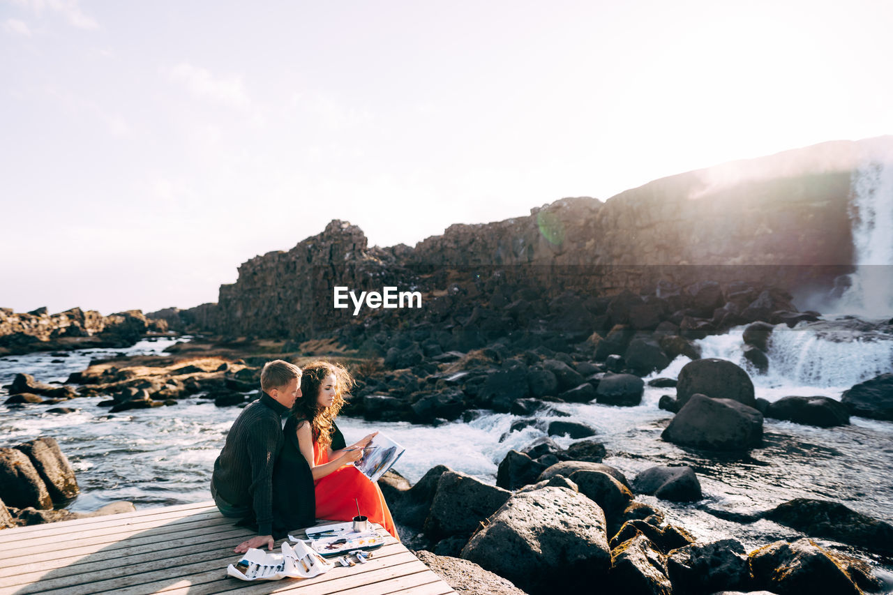 Couple sitting on jetty against sky