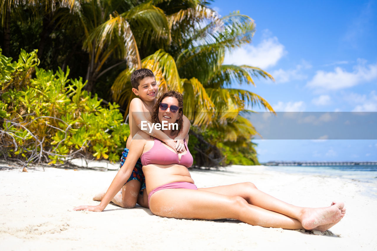 Little kid hugging his mom on a white sand beach