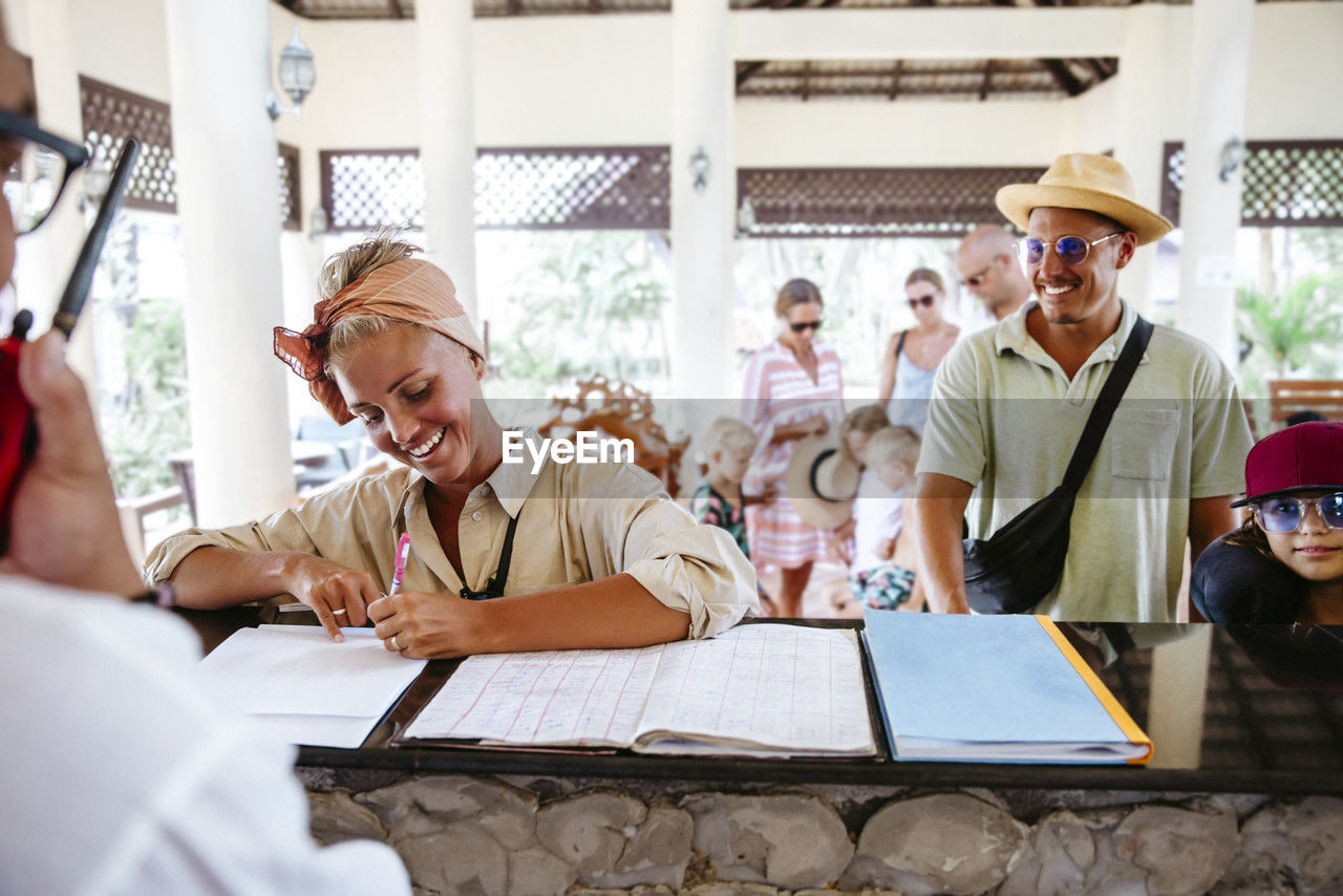 Happy woman signing at reception desk during check in with family at resort