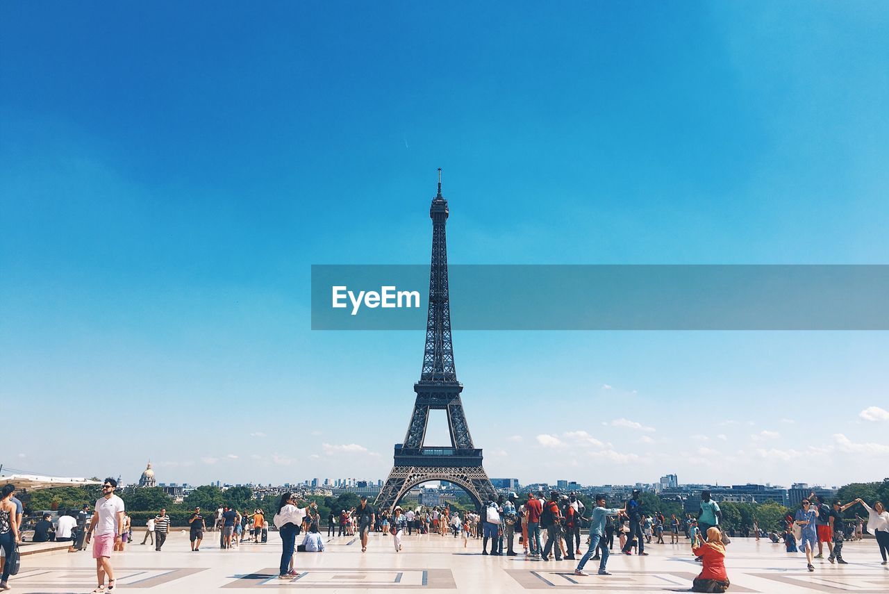 People around eiffel tower in city against blue sky