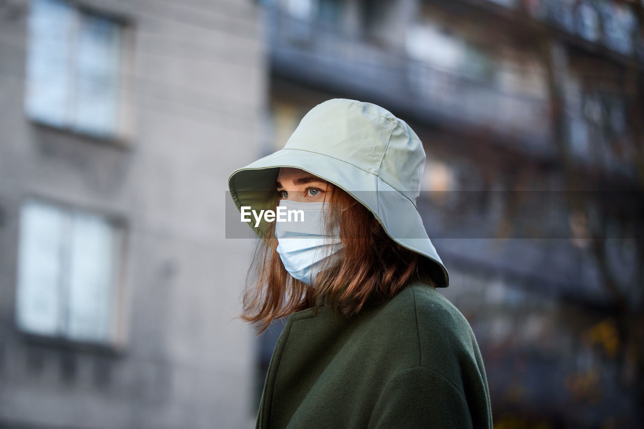 PORTRAIT OF WOMAN STANDING AGAINST BLURRED BACKGROUND