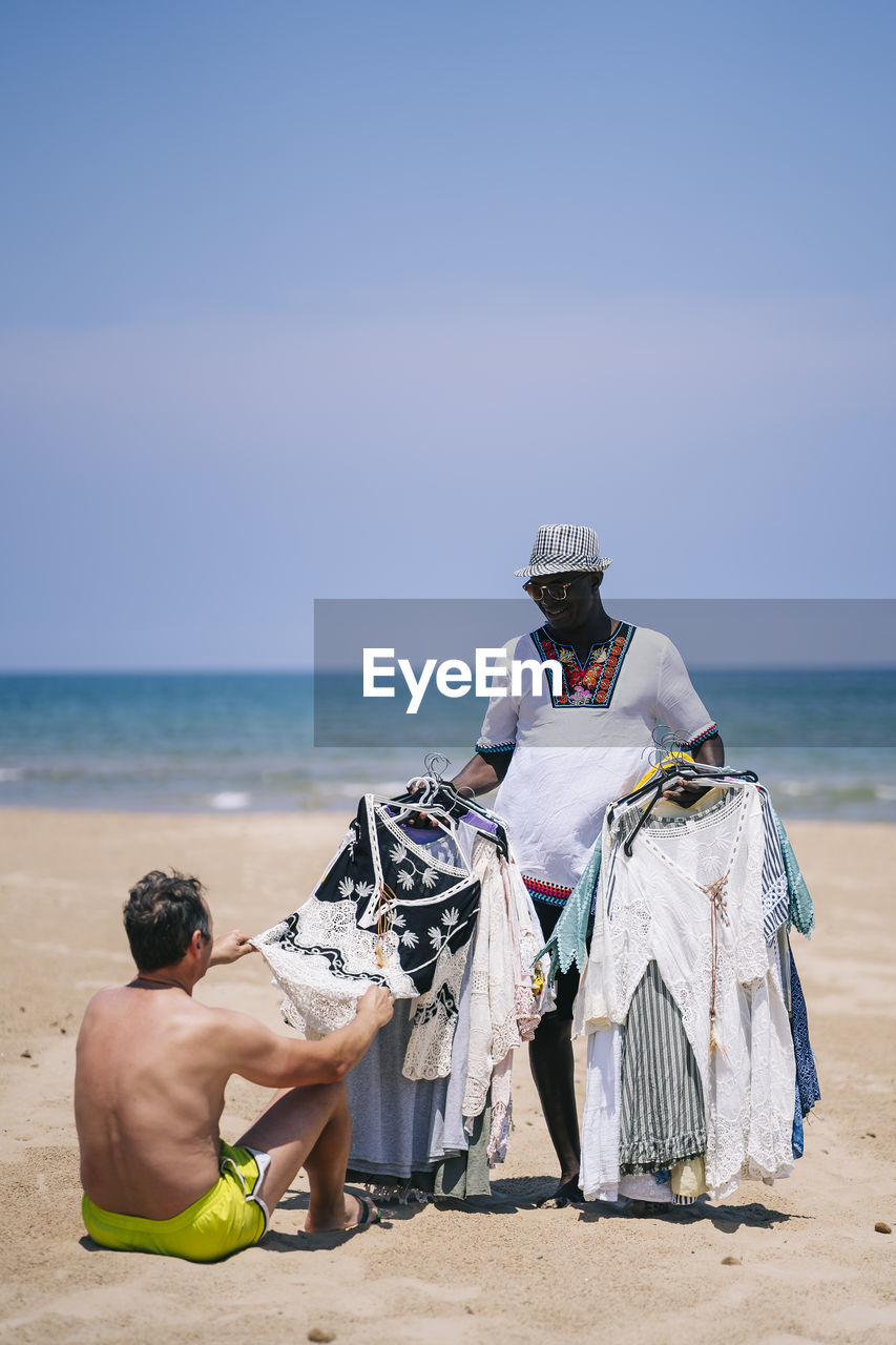 Man buying clothes from male vendor at beach during sunny day