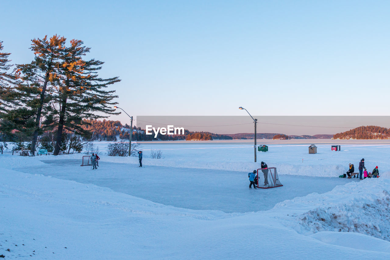 People playing hockey on outdoor ice rink against clear sky during sunset